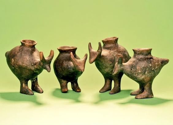 Four small pottery vessels in the shape animal-like figures with round bodies, short legs, and spouted openings. They are arranged on a green background.