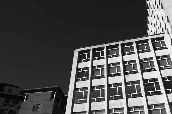 black and white photograph of a pale building seeming made of large windows that are made of smaller windows. the building takes up the bottom right quarter of the frame with the rest dedicated to a dark sky