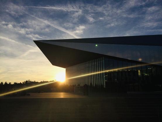 The SwissTech Convention Center, from the side, with the sun setting in the background, right next to it.