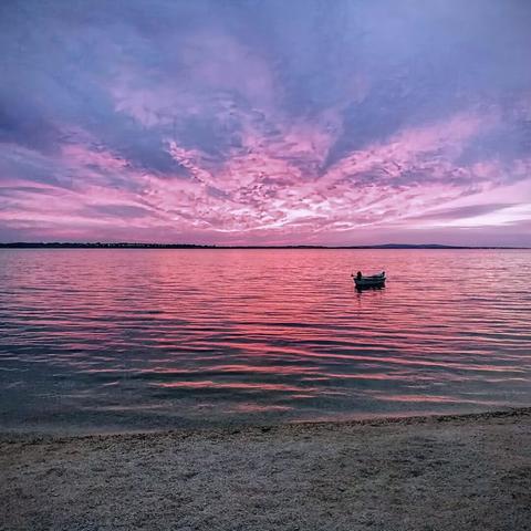 photo of a small boat floating calmly on the ocean during cloudy sunset