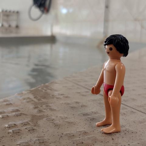 Um playmobil homem de fato de banho está na piscina, pronto para entrar na água