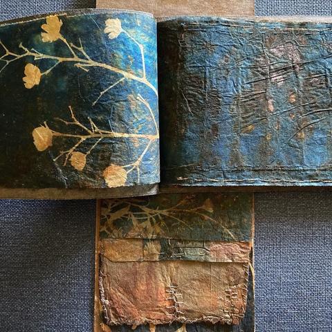 Image of handmade books with pages made from cyanotype printed teabags covered in rust with a waxed paper bag covers. The prints are of leaves and twigs.