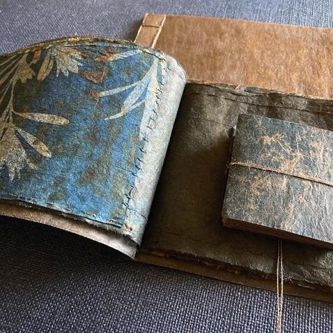 Image of handmade books with pages made from cyanotype printed teabags covered in rust with a waxed paper bag covers.