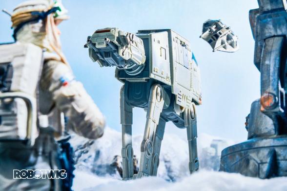 An AtAt approaches. A snowspeeder is flying very close to its rear. A hoth rebel trooper looks on at a closer approaching Atat