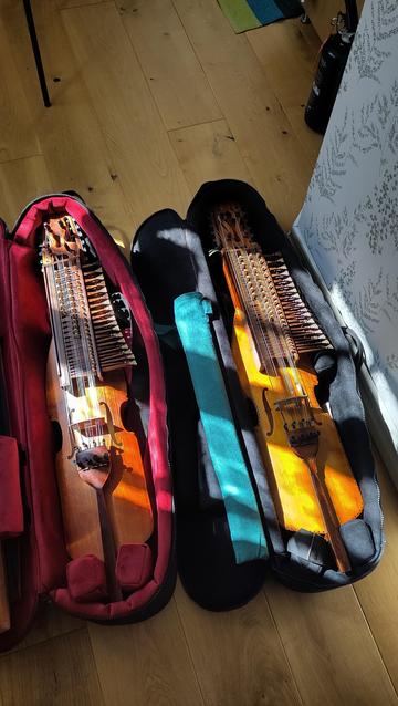 Two instrument cases are lying on the floor, open. In each one there is a nyckelharpa, a traditional Swedish bowed instrument with a keybox made of wooden tangents and a long slim body.
