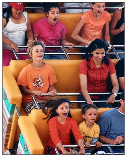 This image captures a thrilling and fun-filled moment of several people riding a rocking ship. The emotions on their faces range from excitement and joy to slight fear and surprise, typical of a high-speed amusement park ride. The wind appears to be blowing their hair, and everyone is securely fastened by safety bars, ensuring their safety while enhancing the ride's thrill. The background is blurred, focusing the attention on the vivid expressions and colorful attire of the riders.