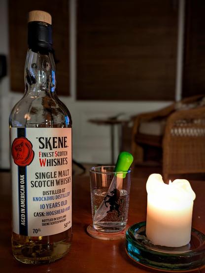A bottle of Knochdhu 10 year old whisky from  Skene on a low wooden table beside a glass of water with a dropper.