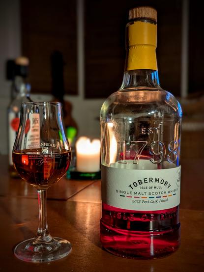 A bottle 10 year old Tobermory whisky on a low wooden table beside a copita glass with a measure of whisky.