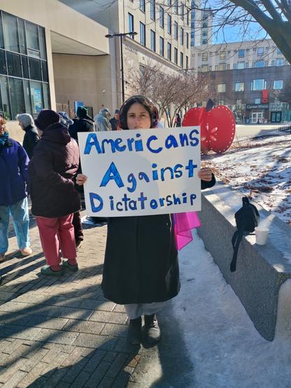 A woman holding a sign that reads: 
Americans Against Dictatorship