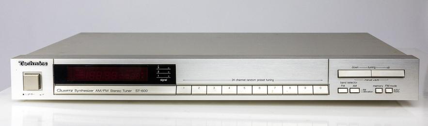 Frontansicht des Radioempfängers als Teil eines Hifi-Anlage. Links der Ein-/Ausschalter, daneben des Display, darunter die Steuerungstasten