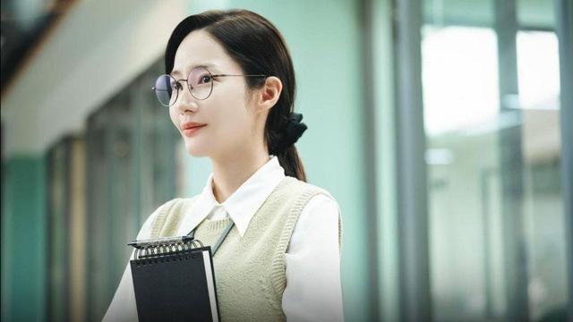 Park Min-young in Marry My Husband k-drama in an white office outfit and glasses. She holds a black binder and smiles
