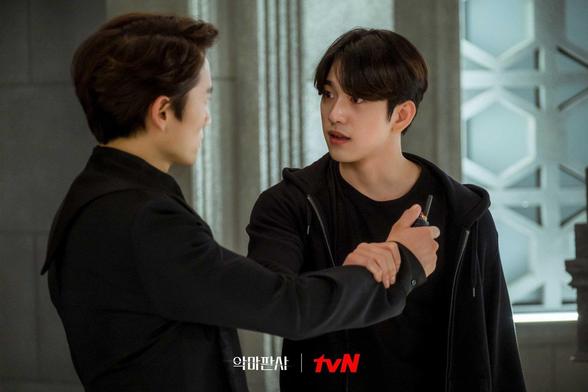 Park Jin-young in The Devil Judge holding Ji Sun's arm in an attempt to stop him from touching him.
They're both dressed in black. A window is behind them