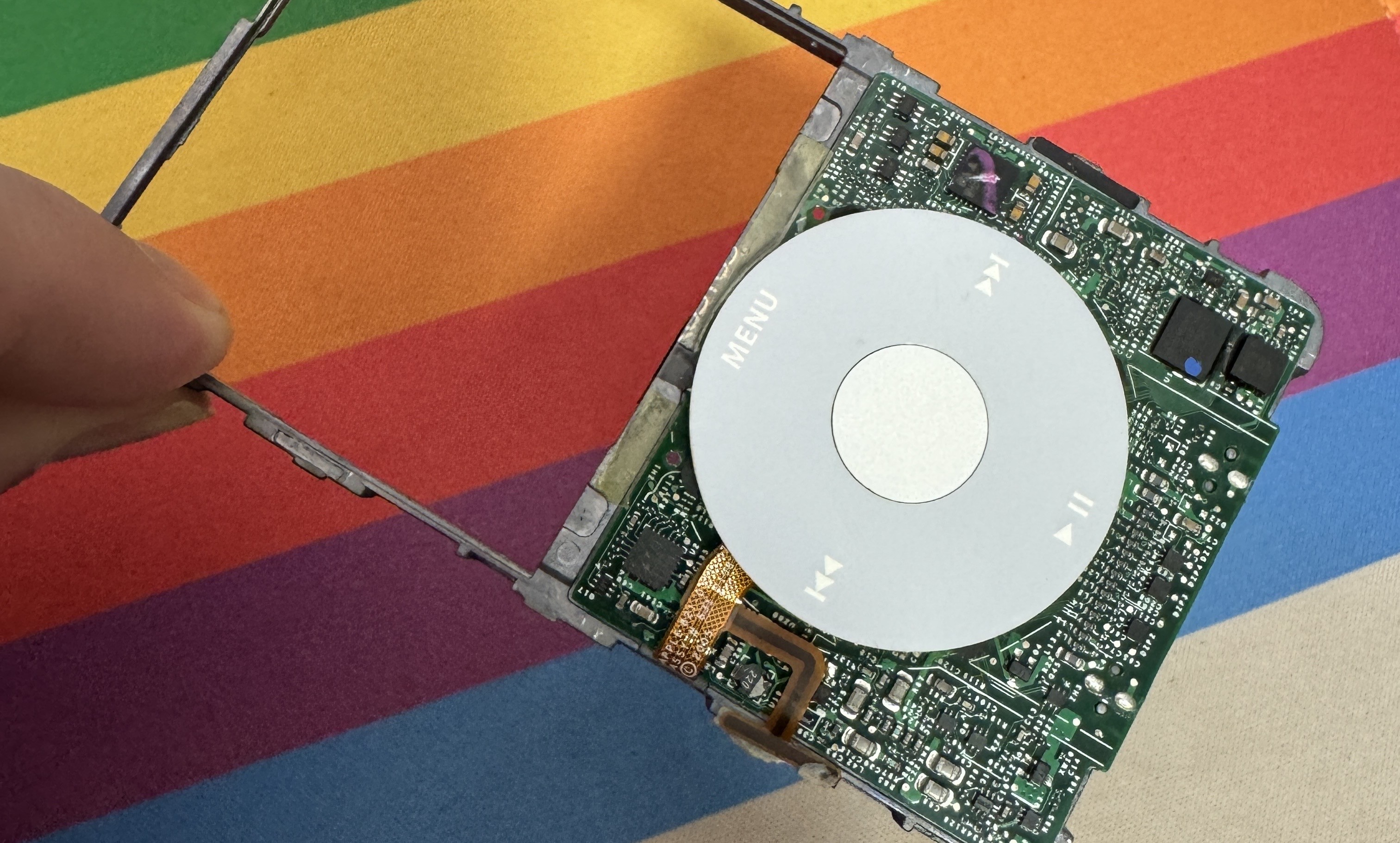 Metal frame and circuit board of an iPod 5.5 gen on top of a rainbow background.