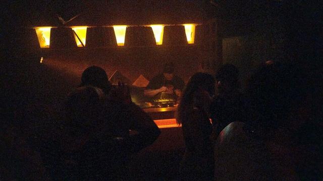 DJ playing vinyl records in a dark club in the background, crowd in foreground