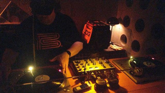 DJ playing records in a darkened club on a rotary mixer.
A recording device and record weight is visible in the foreground.