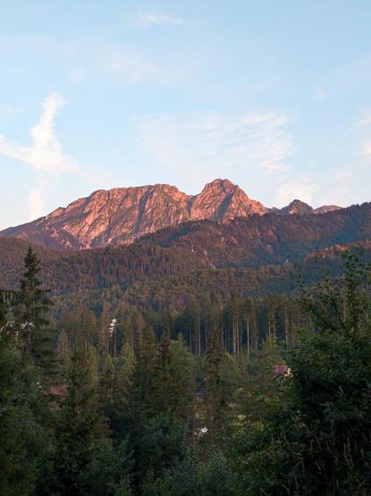 Mountains during sunset, forest all around and white clouds in the light blue sky