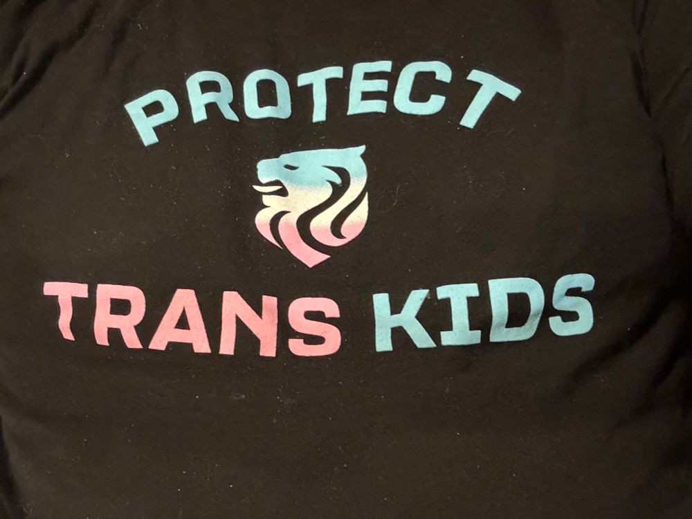 Shirt with text “protect trans kids” and a logo from the Seattle NWSL team, now Seattle Reign.