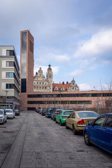 Ein Weg führt den Blick zur Propstei und dem dahinterliegenden neuen Rathaus von Leipzig. Im Bild ist am linken Rand das Bürogebäude der Caritas und hellblauer Himmel mit weißen Wolken zu sehen.