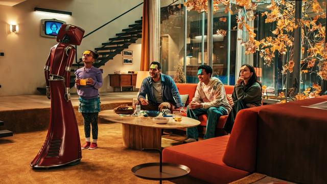 Familie mit rotem Haushaltsroboter "Cassandra" im Retro-Zukunftsdesign der 70er-Jahre auf einem Artwork der gleichnamigen Netflix-Miniserie. Die Personen befinden sich in einem weitläufigen Wohnzimmer mit großen Fenstern und herbstlichem Baum im Hintergrund. Auf einem Monitor an der Wand ist zusätzlich Cassandras computergeneriertes Gesicht zu sehen. Der Farbton der Szene ist sehr warm.
