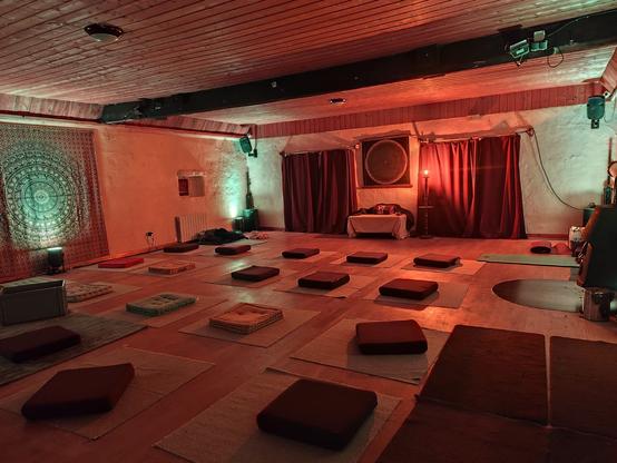Salle vide avec nombreux coussin et tapis pour méditer, lumière tamisée, rideaux et tentures au mur et poêle à bois.