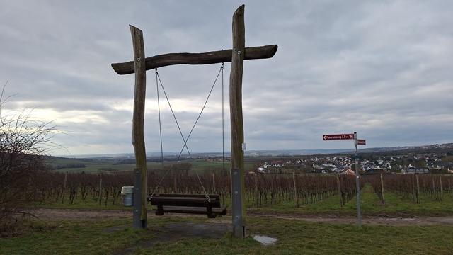 Eine große Schaukel mit dem Dorf Klein-Winternheim im Panorama/ a big swing with the wine village Klein-Winternheim in panoramic view