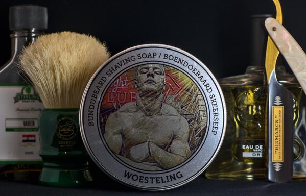 (ChatGPT description)

A bold and rugged wet shaving setup is displayed against a dark background. At the center, Bundubeard Woesteling shaving soap features striking artwork. A Bismarck straight razor with a pearlescent handle stands beside a classic glass bottle of cologne. A Zenith boar brush with a green handle sits next to a Stirling Soap Co. Varen aftershave. This collection exudes strength and tradition, blending vintage aesthetics with modern grooming essentials.