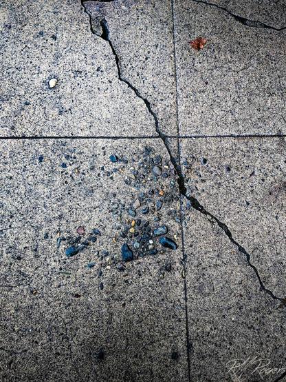The rough interior stone aggregate is exposed on a small section of sidewalk, combined with lines and cracks, forming a pleasing composition.