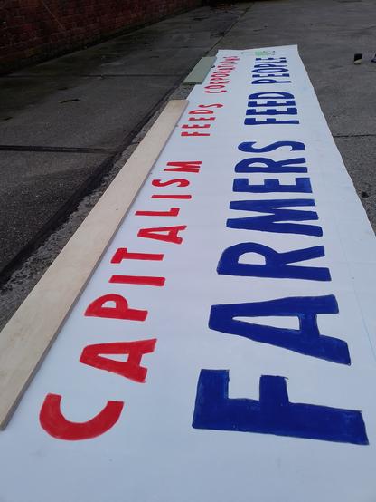Een net geschilderde banner op de grond. De tekst erop is 'Capitalism feeds corporations, Farmers feed people'