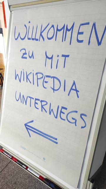 Ein weißes Flipchart, auf dem mit Marker „Willkommen zu mit Wikipedia unterwegs“ geschrieben ist.