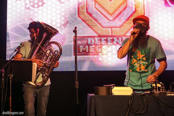 special guest ap0c (pronounced "A-poc") plays tuba while Defense Mechanism holds a microphone