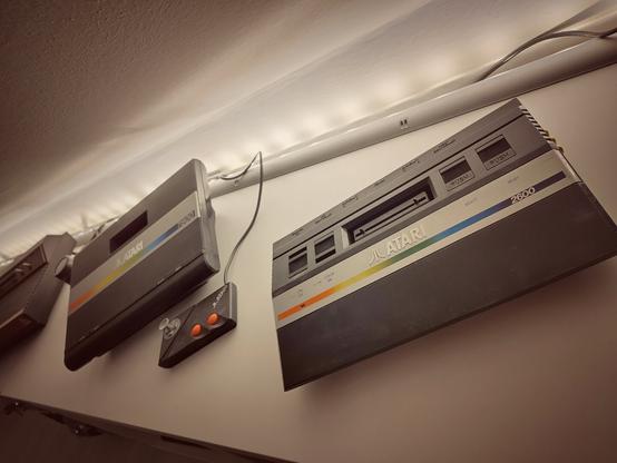An Atari 2600 jr. in the foreground and a 7800 in the background, placed on a shelf