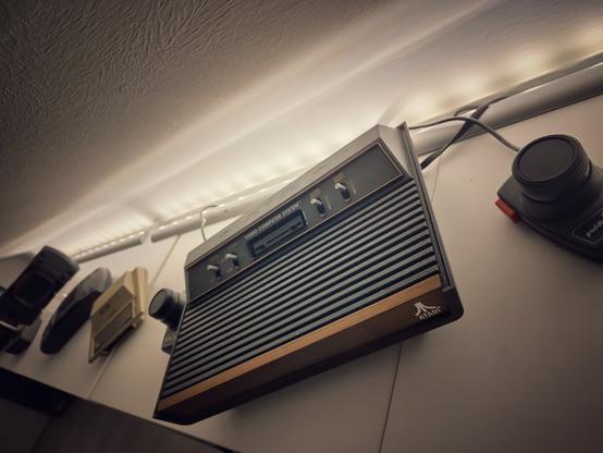 An Atari VCS and two paddle controllerin the foreground and a Atari 400 Mini in the background, placed on a shelf
