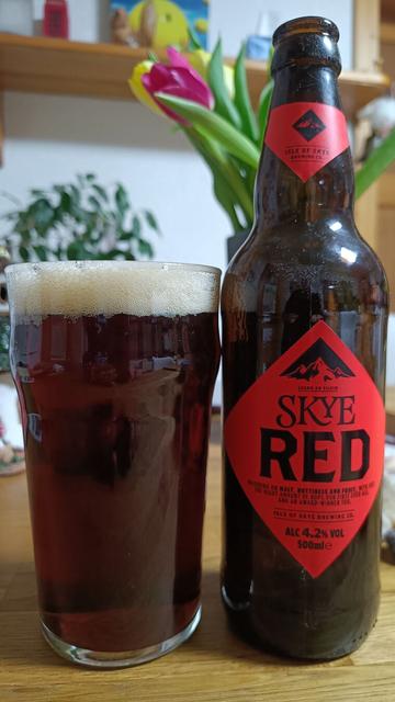 auf einem Holztisch steht eine Bierflasche mit rotem Etikett und Aufschrift "Skye Red" und daneben ein mit braunem Bier gefülltes Glas