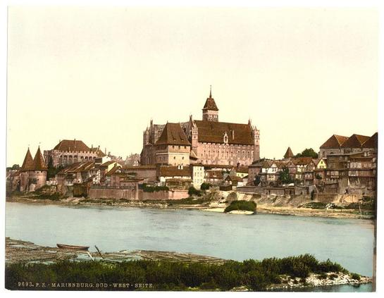 This image depicts a historical scene featuring Marienburg, located on the southwestern side in what was then Prussia but is now Malbork, Poland. The focus of this photograph is an expansive view of the medieval castle that dominates the skyline. This fortress has multiple towers and spires, reflecting Gothic architectural elements from its era.
The surrounding area shows a mixture of residential buildings with pitched roofs and various structures indicative of life during or before modern times. In the foreground, we see a riverbank where boats are moored to wooden poles in shallow waters amidst green vegetation at water's edge.
To provide context for this historical image: It appears as though it was taken between approximately 1890 and 1900 based on its characteristics which include sepia-toned colors reminiscent of early photographic processes. The photograph captures a moment frozen in time, showcasing the architectural grandeur of Marienburg amidst an environment that tells us much about daily life during this period.
This image is noteworthy for being part of Loener's Photochrom Prints collection available at Views of Germany (https://images.loener.nl/PhotochromPrints/full/65e4/65e47ab45890ae069f680352.jpg), indicating its historical value and interest. The landmark status, detailed description provided here along with the source link to find more information about this specific image helps in understanding and ap [...]