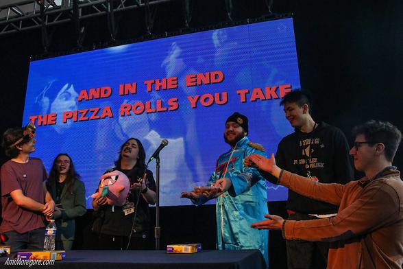 Assembled members of SiIvagunner standing in front of a video screen that says, "And in the end the pizza rolls you take" as Larry holds a tupperware full of Totinos