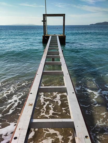 symmetrischer Bootsanleger ragt ins türkise Meer.