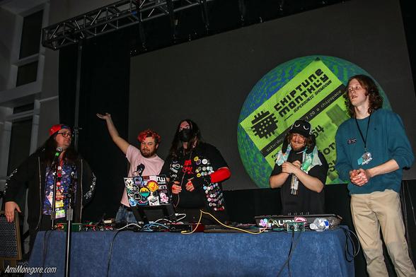 From left to right
Adam Seats, Donutshoes, Petriform, Maxo, Dorkus64 posing in front of a Chiptune Monthly graphic