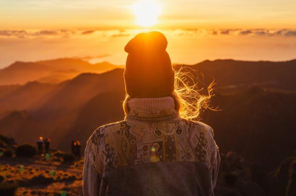 Woman standing with her back to the lens, sunrise, clouds and mountains in the background