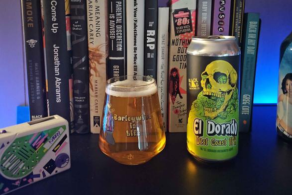 A stemless wine glass filled with beer and a 16 ounce can sit on a shelf. The glass features art of a Manatee wearing a crown, sweater and chain to look like Biggie Smalls. The text says "Barleywine Is Life". The can art show a skull sitting on a mountain of hops, with hops coming out of the eye and nose sockets, and the mouth. 

Behind are some books about various music genres (80's rock, hip hop), music artists (2Pac, Aaliyah, Mariah Carey, etc.), and sports (All The Smoke, Stugotz, Greg Cote), as well as a soju bottle featuring Hyori, and a Pocket Rocker.