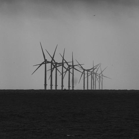 A black and white photo of a row of wind turbines out to sea