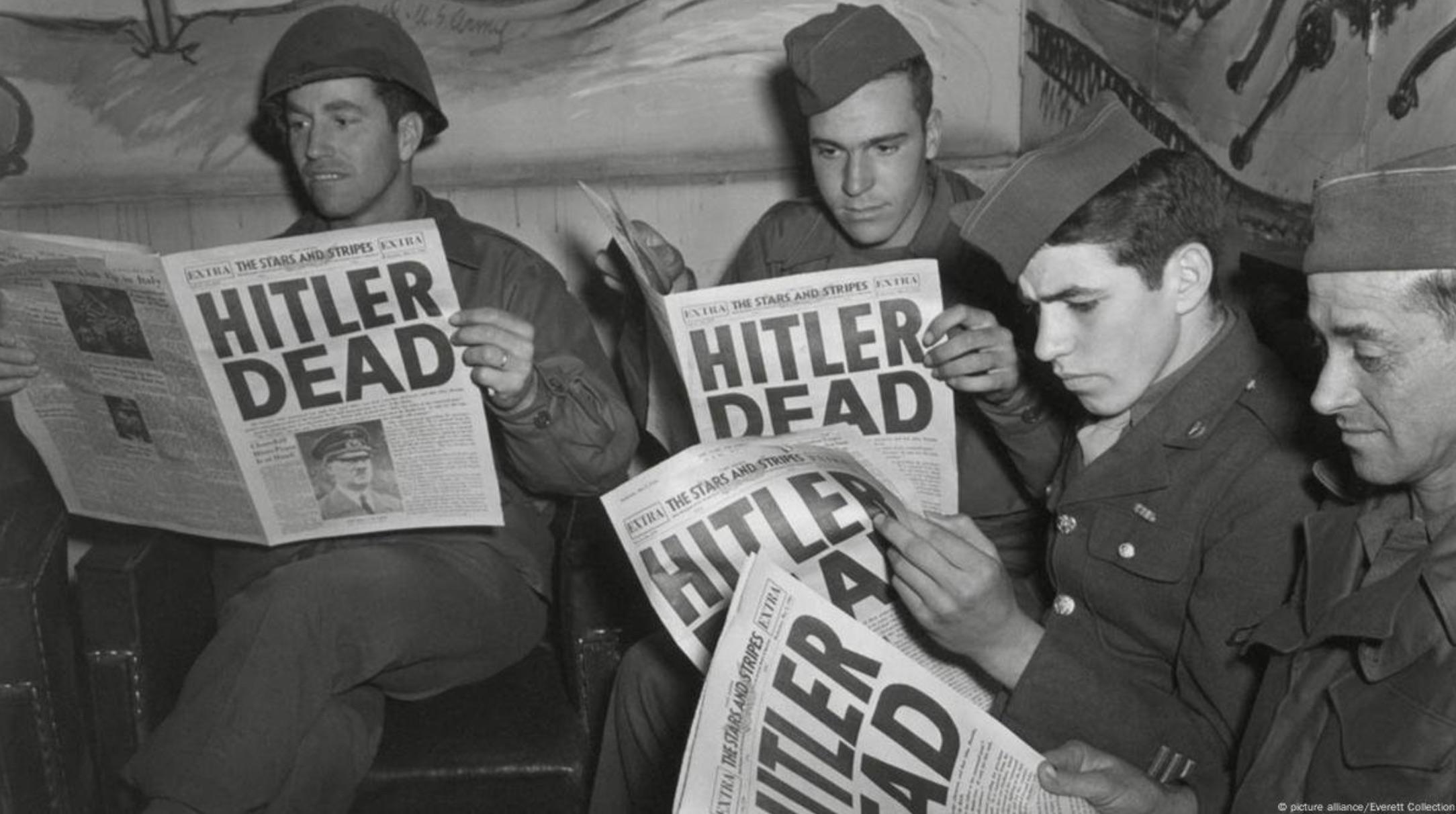 A group of soldiers reading newspapers with the headline: HITLER DEAD