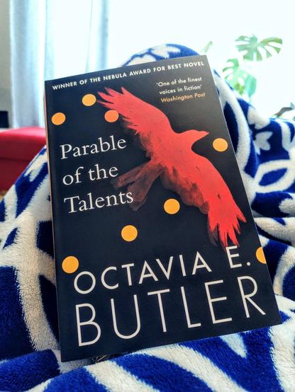 A paperback copy of Parable of the Talents by Octavia E. Butler on a blue and white fleece blanket.