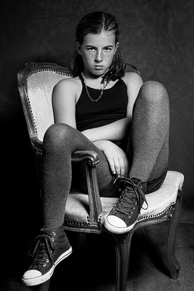 10-year-old girl, lounging in an armchair and looking intensely into the camera.