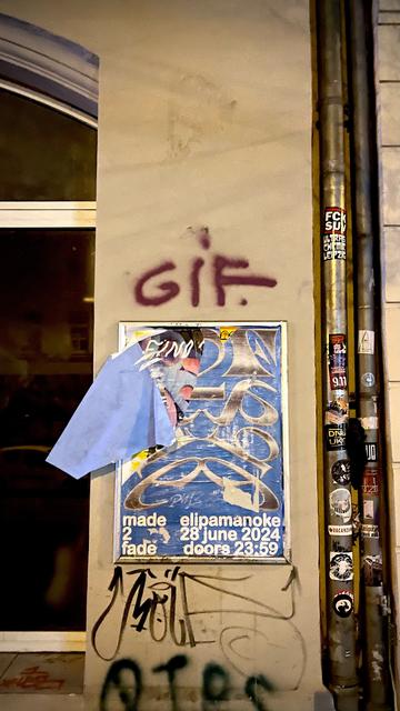Photo of a wall on a street in Leipzig. There is a poster of a show and above it graffiti of the letters GIF