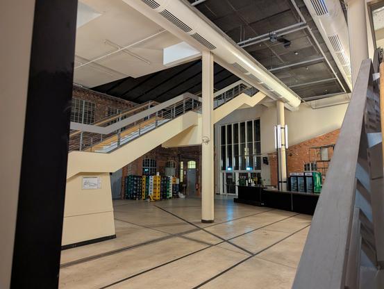Interior shot of a cinema building. The large hall has stairs going from the ground floor to the second floor; white ceilings and an open space below it.