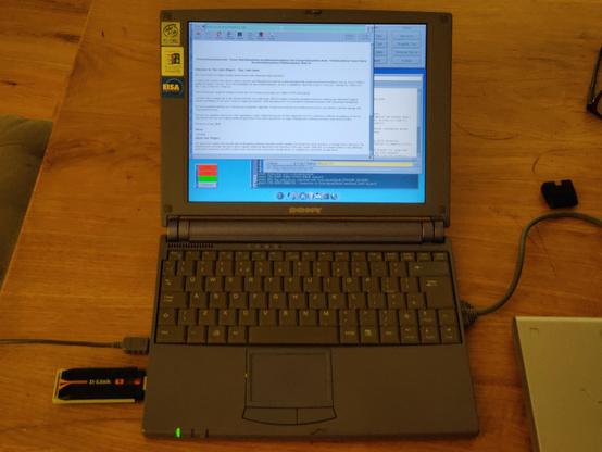 A landscape photo in artificial light of my Sony VAIO PCG-N505X with the PCMCIA CDROM plugged in on one side and a chonky D-Link WiFi USB stick on the other.

The screen is showing several overlapping windows. The top one is the Dillo browser displaying the Tiny Core homepage.