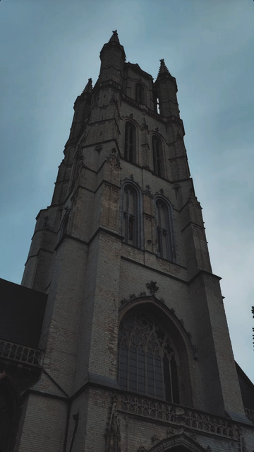 The greyish white outside of the gothic St Gabo cathedral in Gent. The facade is made of brick, there is a big gothic window.