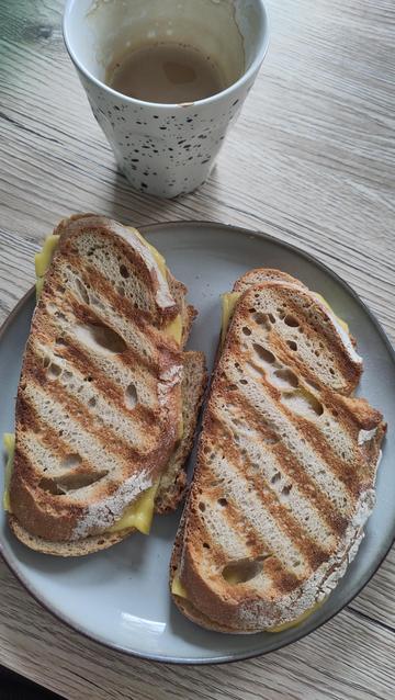 Two servings of grilled cheese, or what they call croque monsieur here on a grey plate on a wooden table. We made a vegan version of it! There also is some coffee in a white cup with black speckles.