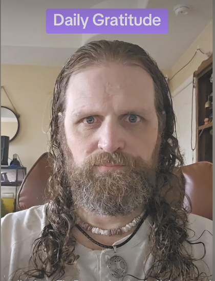 A white man in his 40s, who bears an unfortunate resemblance to Charles Manson, appears to glower straight into the camera, with an expression he probably believes is "compassionate sincerity" or something. His slightly unkempt beard and long, greasy (I think wet, actually) dirty blonde hair frame his shell necklace and some kind of medallion on a leather thong. I'm saying he looks fucking creepy.

There is a banner above his head reading "daily gratitude."