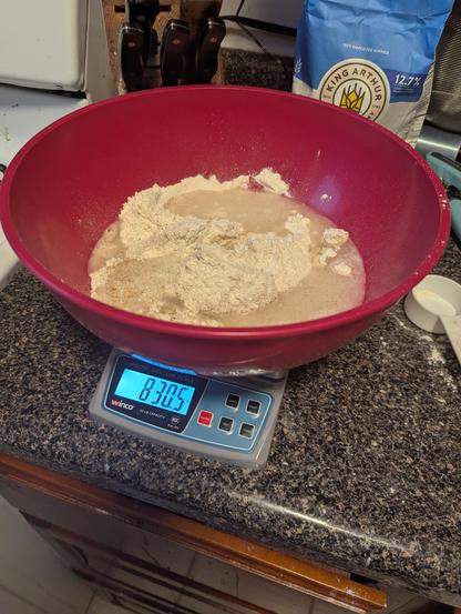 A big red bowl, on a scale with flour and water in it, flour bag behind.